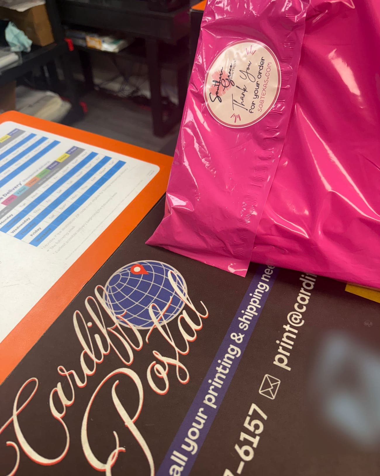 A bright pink poly mailer with a boutique sticker on the Cardiff Postal counter mat