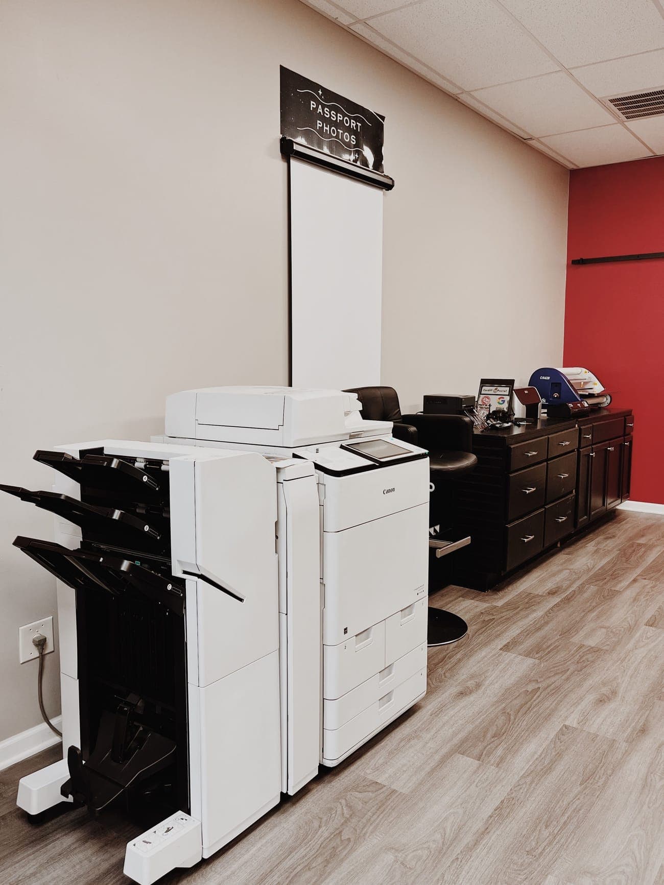 A production copier with a finisher beside the white passport photo backdrop