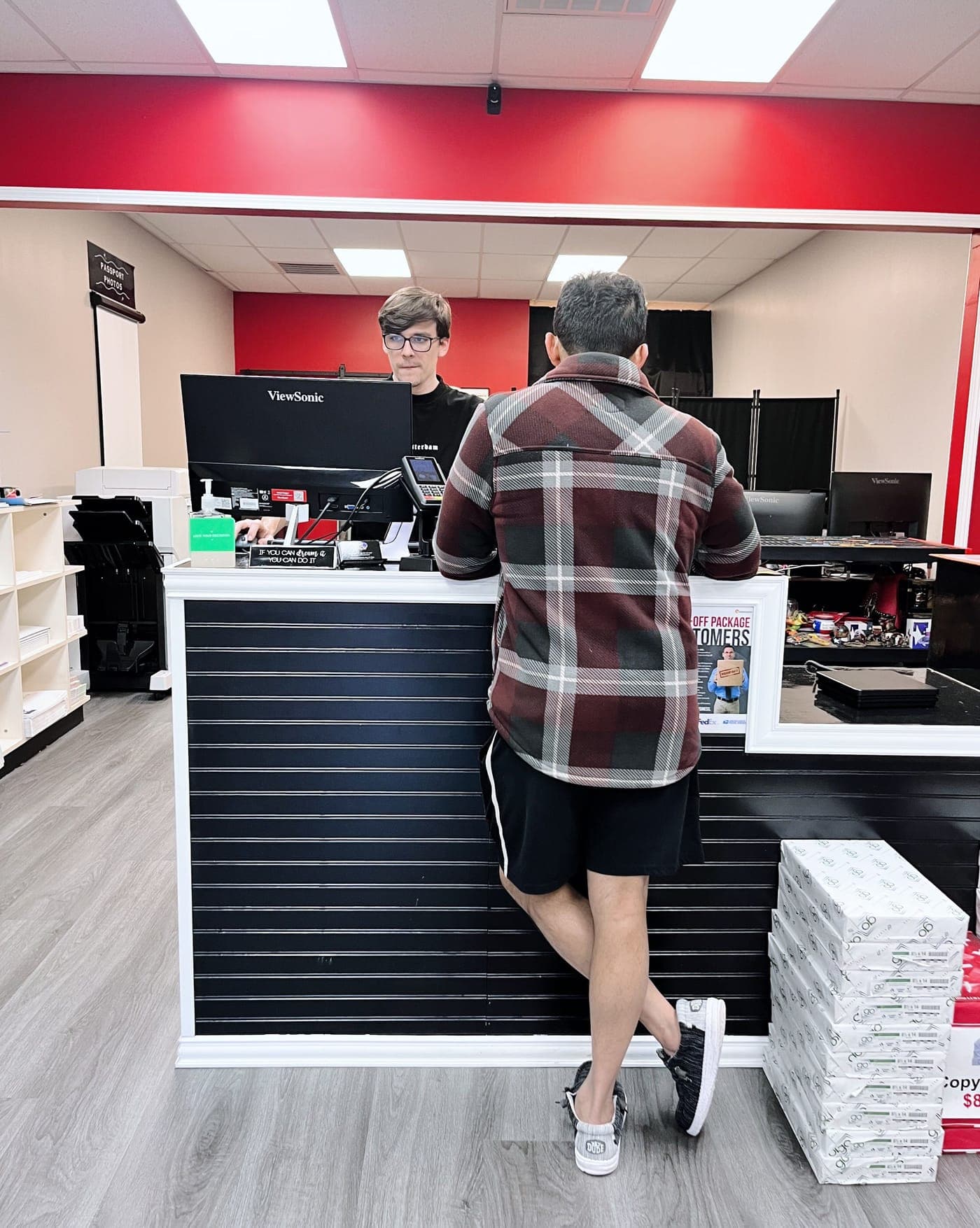 A customer at the black slatwall front counter while a team member helps behind the monitors