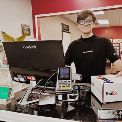 A smiling Cardiff Postal team member at the front counter with a FedEx box ready to ship