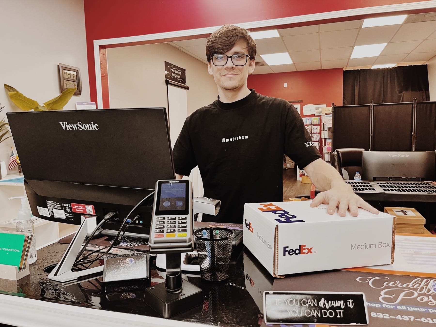 A smiling Cardiff Postal team member at the front counter with a FedEx box ready to ship