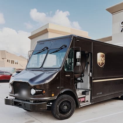 The Cardiff Postal storefront on FM 1463 with its lit sign, Pack . Ship . Print & More, and a brown UPS package truck parked at the entrance