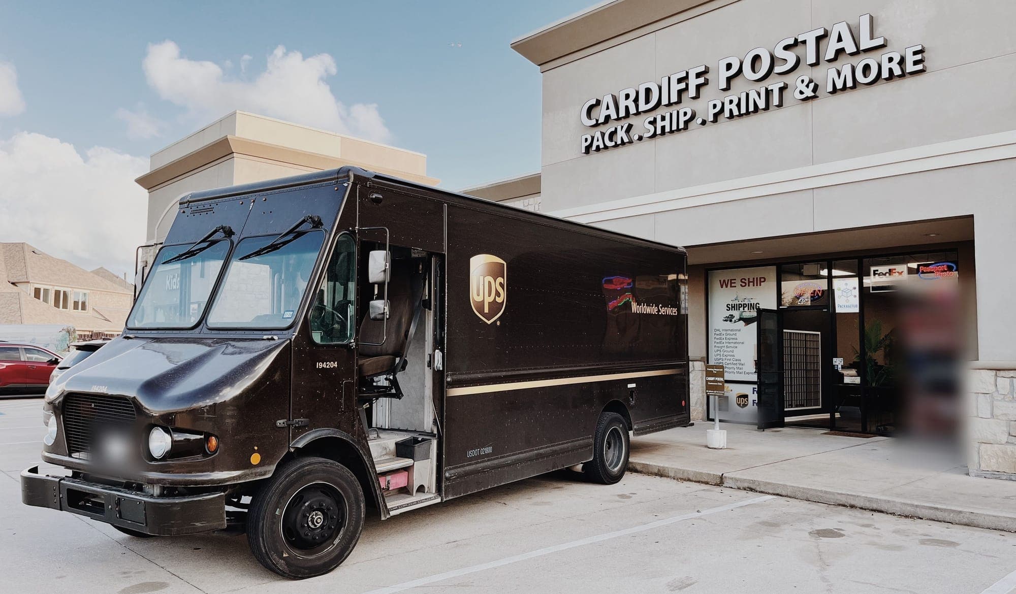 The Cardiff Postal storefront on FM 1463 with its lit sign, Pack . Ship . Print & More, and a brown UPS package truck parked at the entrance