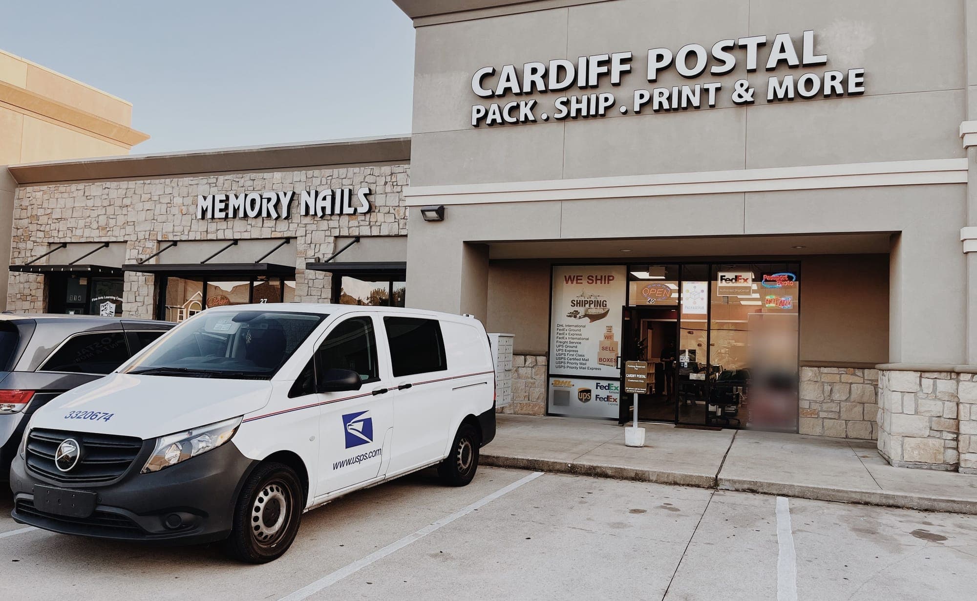 A white USPS delivery van parked in front of the Cardiff Postal storefront