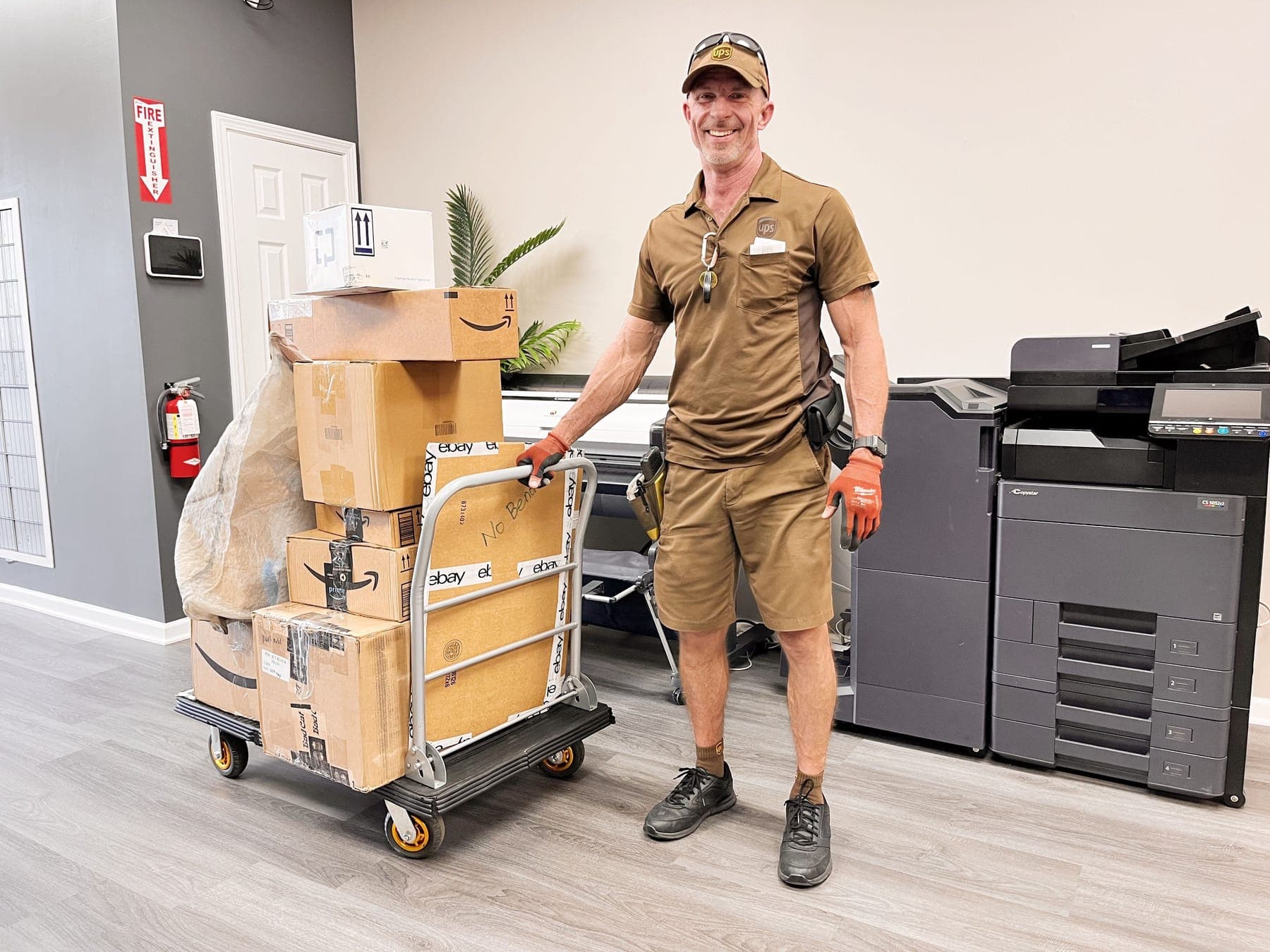 A UPS driver inside the store next to a hand truck stacked high with boxes ready to go out